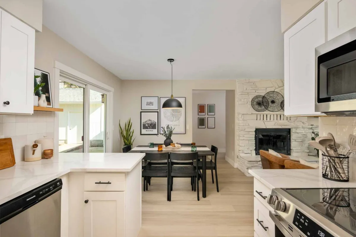 A cozy view of the dining area with a dining table and kitchen island, accented by a warm fireplace and inviting wall art. The space is arranged for gatherings, meals, and entertaining guests, seamlessly blending dining and cooking spaces.