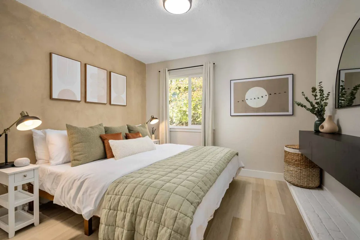 A serene bedroom featuring a bed with a green quilt and decorative pillows, artwork on the walls, and a window that allows abundant natural light to fill the space. The overall ambiance is peaceful and cozy, ideal for restful sleep and quiet moments of relaxation.