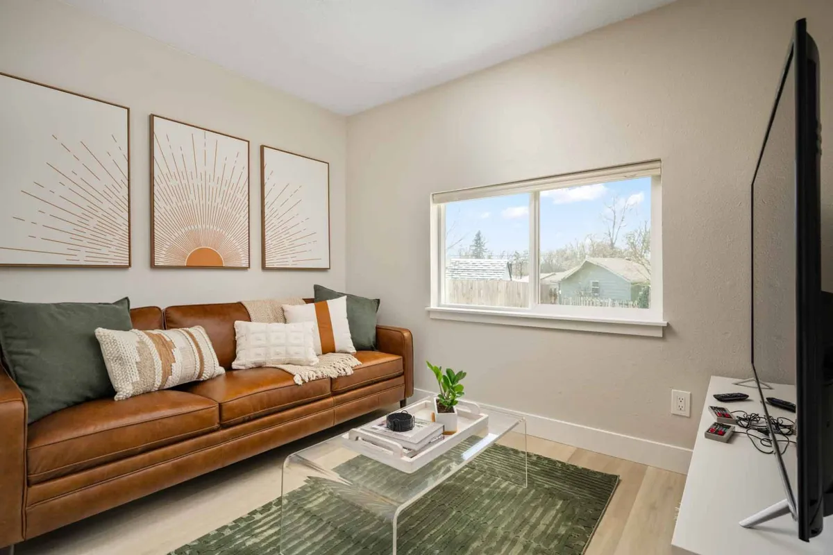 A comfortable living area featuring a brown leather sofa, decorative wall art, and a window with an exterior view. The scene exudes both relaxation and sociability, suggesting a place to unwind, read, or socialize after a commute.