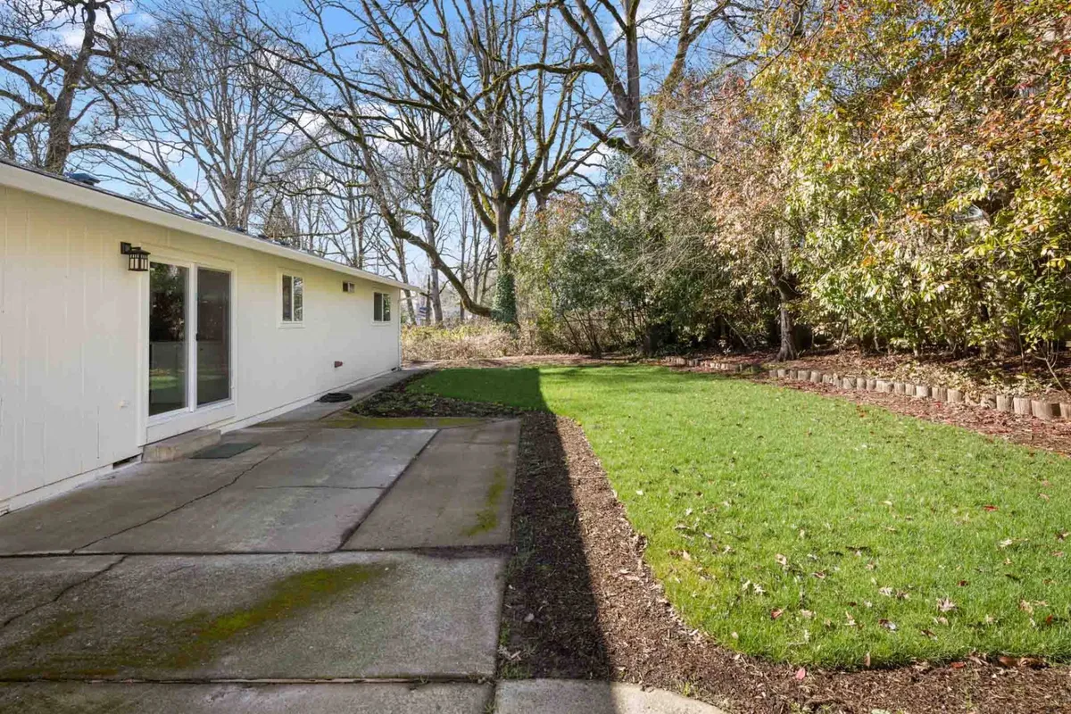 A peaceful patio area sits amid a green, well-maintained lawn and is framed by tall, leafy trees. This secluded outdoor nook invites moments of relaxation—whether meditating at sunrise, enjoying coffee, or letting pets roam safely in the grass.