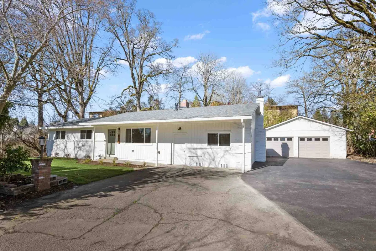 This image showcases the white exterior of The Holistic Hideaway, with a spacious driveway and lush surrounding trees. The inviting porch and ample parking area are visible, suggesting ease of access for families and guests arriving after a day of local adventures.